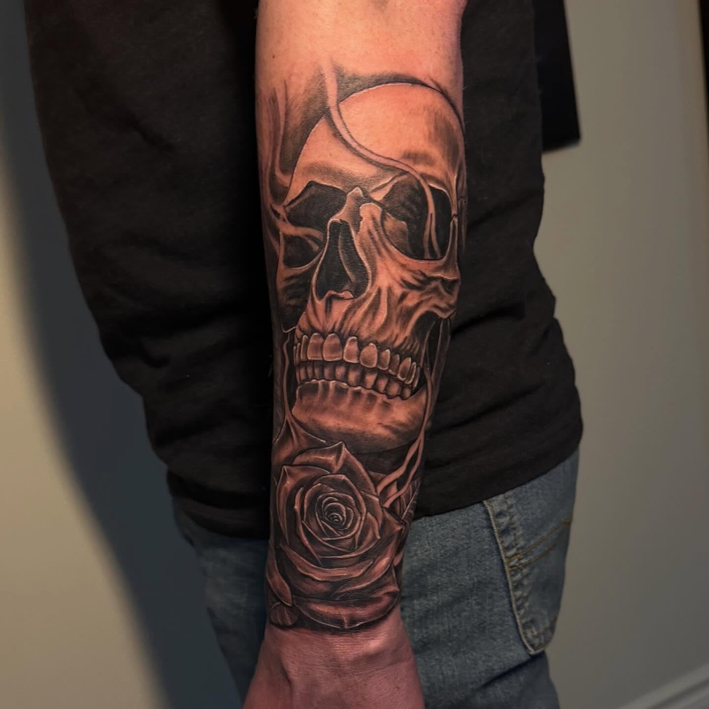 Detailed skull and rose black and grey tattoo on forearm