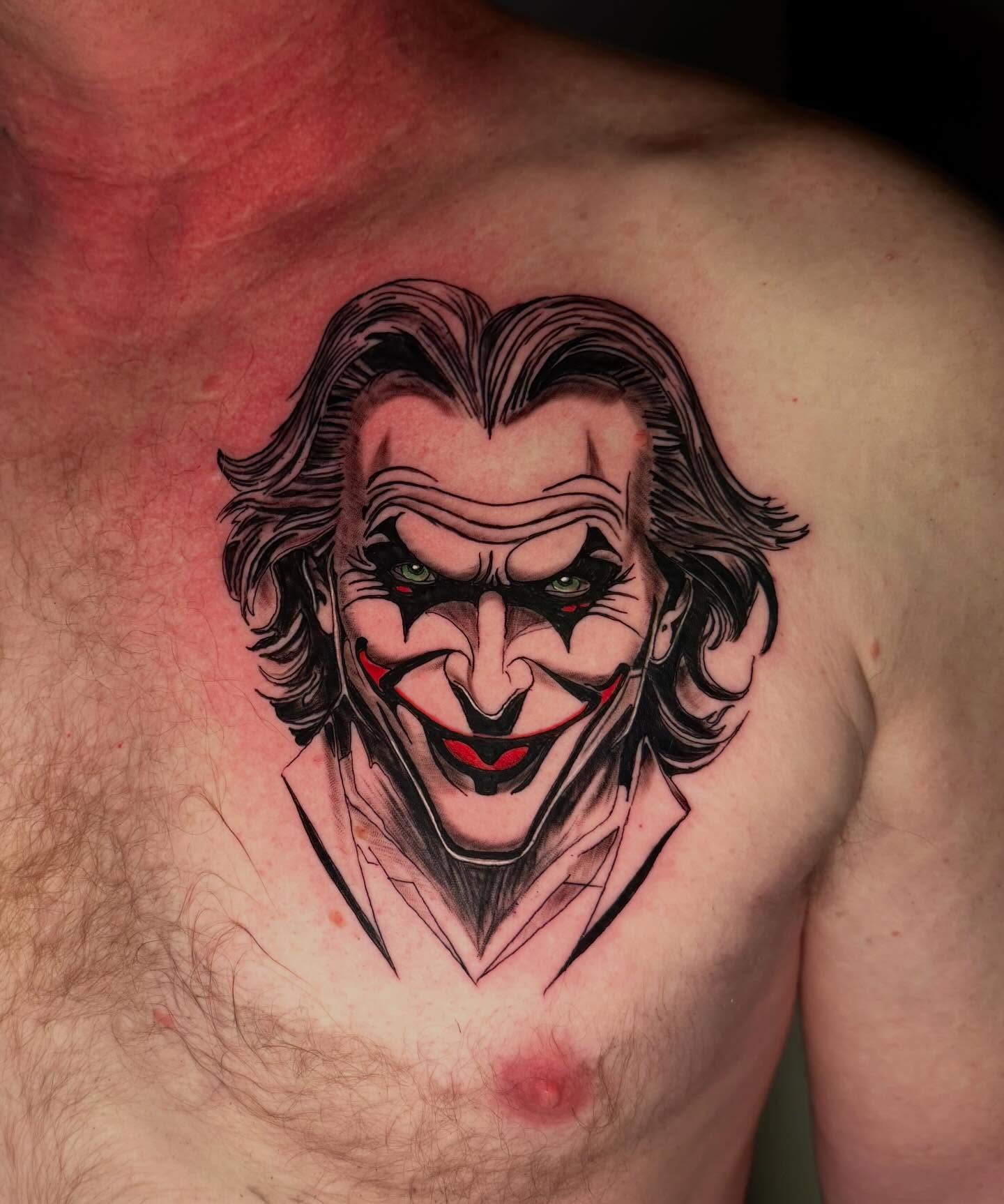 Vivid graphic Joker chest portrait tattoo with green eyes and red mouth outline